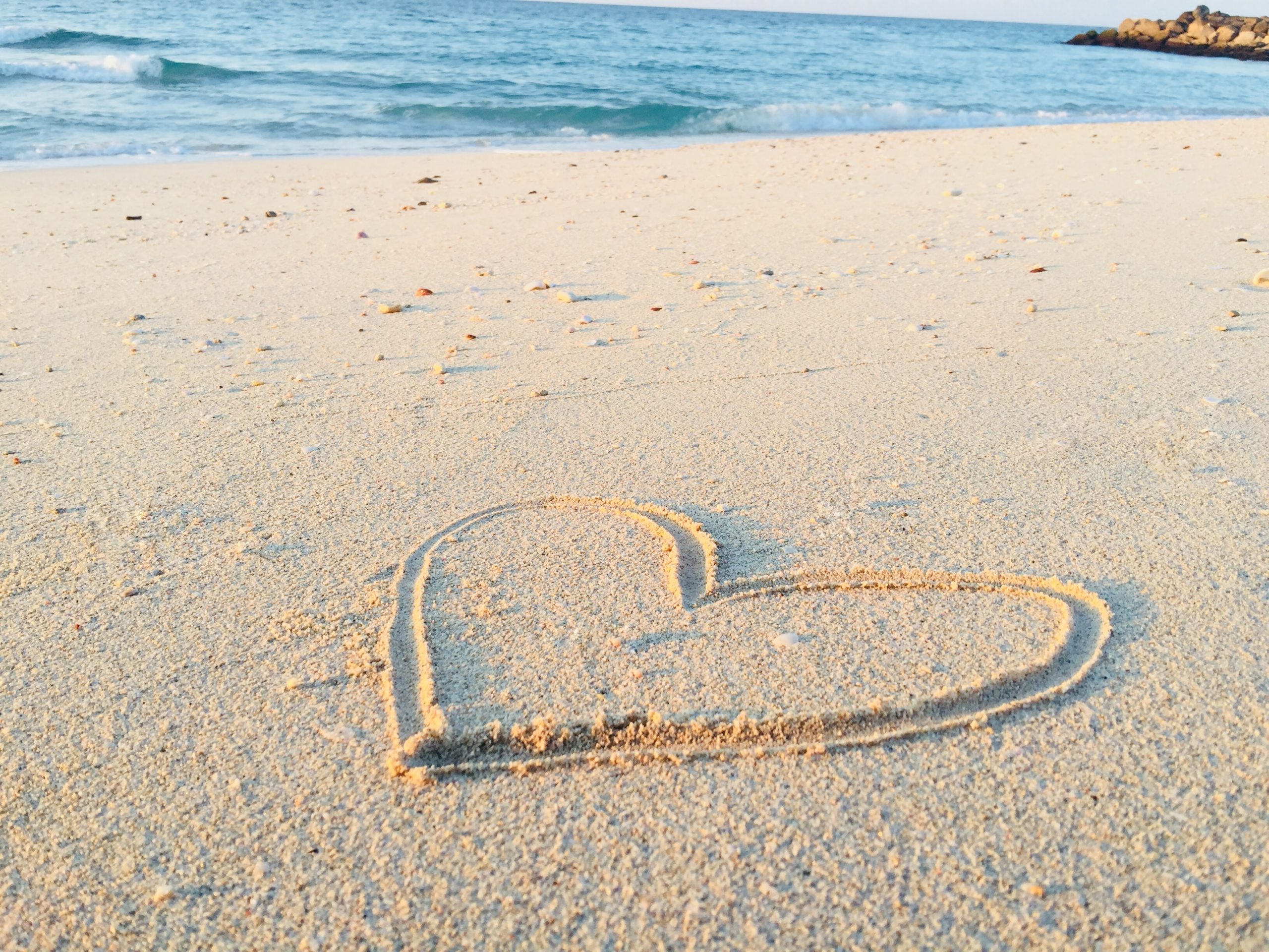 A sandy beach with waves visible in the distance, in the foreground a love hearts is drawn in the sand.
https://unsplash.com/photos/FHT0KEOwtyg